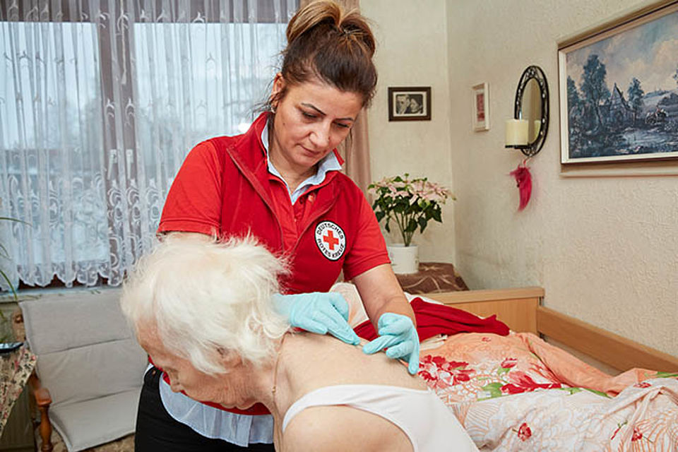 Wundversorgung DRK-Pflegekraft versorgt eine Wunde auf dem Rücken einer älteren Dame