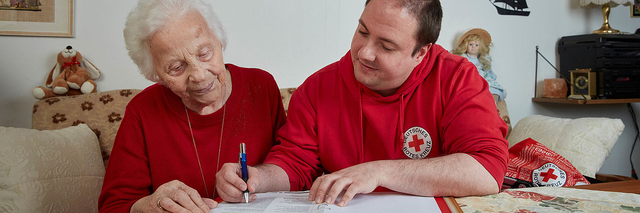 Beratungsgespräch DRK-Mitarbeiter und ältere Dame sichten Informationsunterlagen